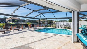 A covered outdoor swimming pool area with lounge chairs and a view of a marina. - Enchanting, this four-bedroom, three-bath home promises stunning sunset views every evening. (Marco Island)
