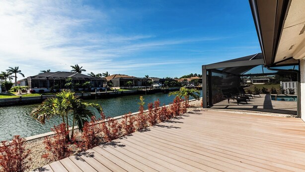 A modern waterfront property with a wooden deck, a pool, and a view of the marina. - Enchanting, this four-bedroom, three-bath home promises stunning sunset views every evening. (Marco Island)