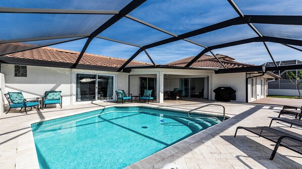 A swimming pool with a covered patio area, including chairs and a barbecue grill.
