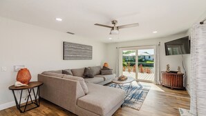 A modern living room with a sectional sofa, a coffee table, and a view of a garden through glass doors. - Enchanting, this four-bedroom, three-bath home promises stunning sunset views every evening. (Marco Island)