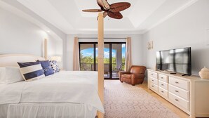 Een slaapkamer met een bed, een televisie, een stoel en een balkon met gordijnen.