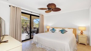 Une chambre d’hôtel comprenant un lit, deux tables de chevet avec des lampes, un ventilateur de plafond, une grande fenêtre avec des rideaux et une vue sur l’extérieur.