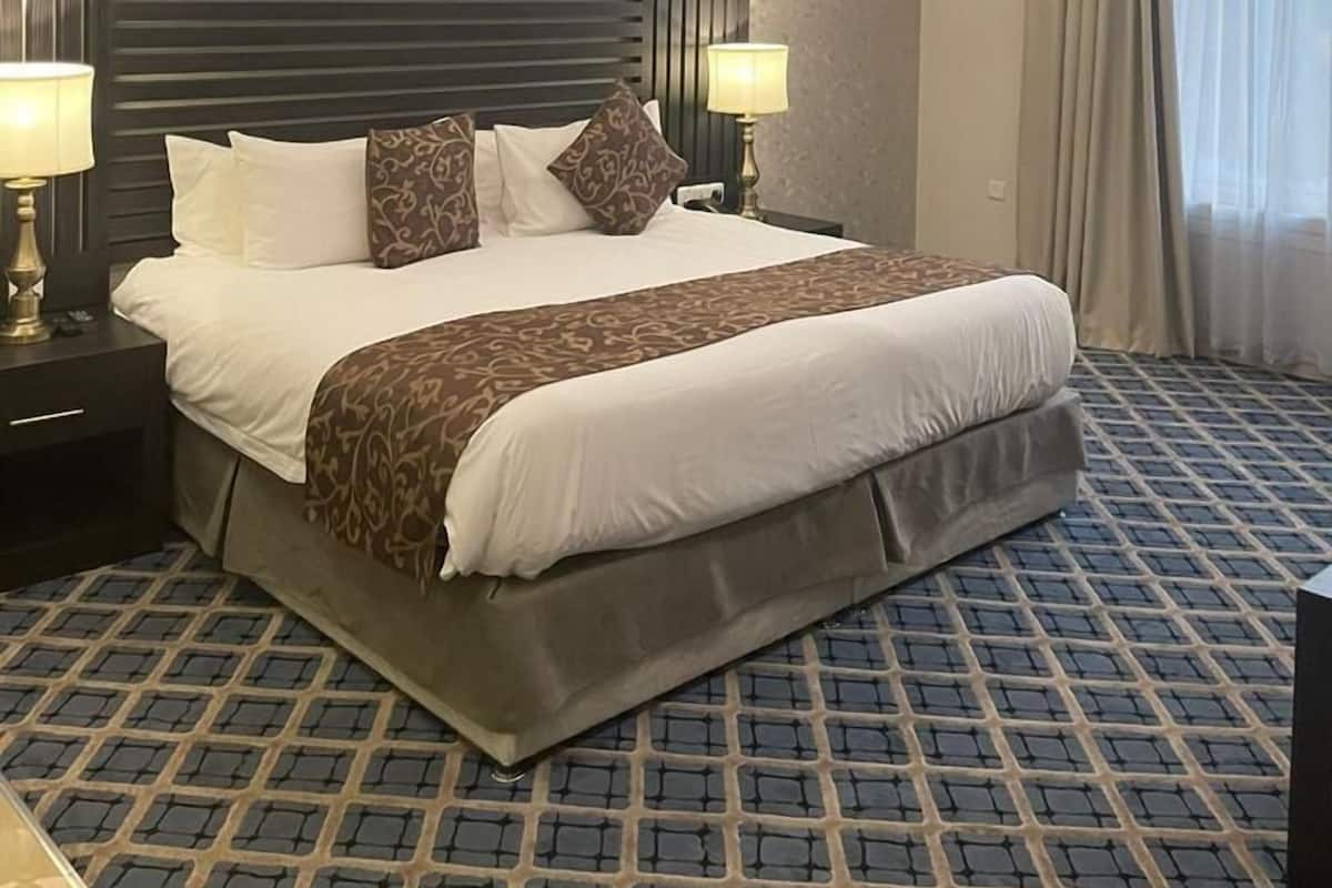 A hotel room with a large bed, two bedside tables with lamps, a headboard, and a patterned carpet.
