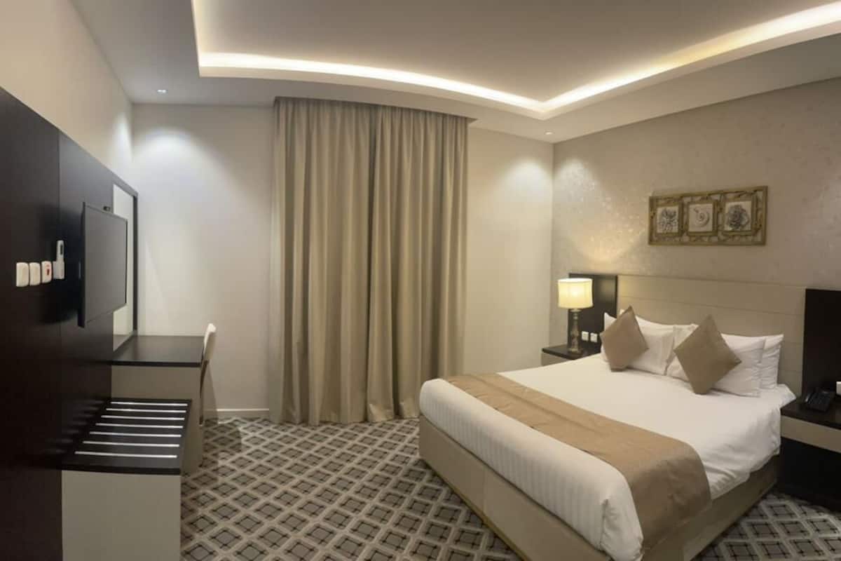 A hotel room with a bed, a desk, a chair, a TV, and a curtain.