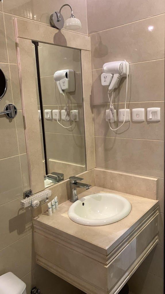 Un baño con lavamanos, espejo y dos secadores de pelo fijados a la pared.