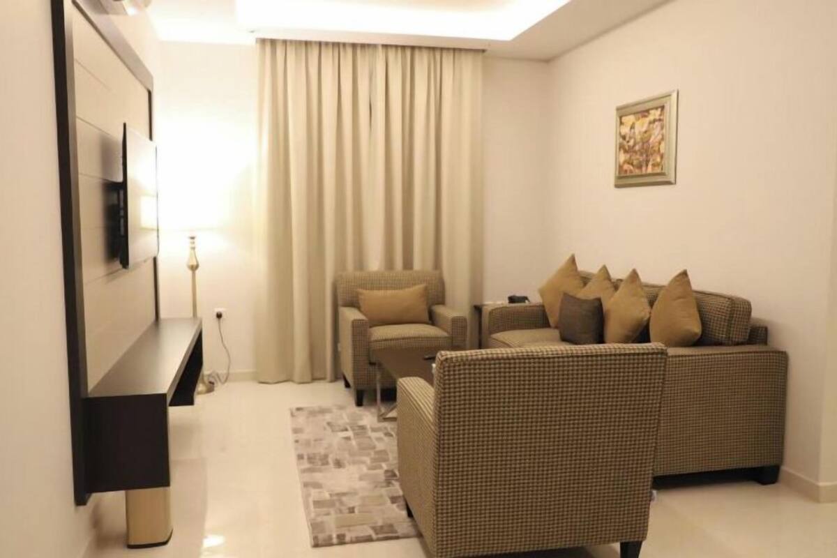 A living room with a sofa, a chair, a flat-screen TV mounted on the wall, and a lamp.