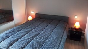 Una cama bien hecha con una colcha estampada, dos lámparas de noche y una mesita de noche pequeña con una lámpara.