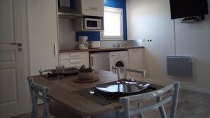 Cocina compacta con microondas, horno y lavadora. Hay una mesa de comedor con sillas y una pequeña planta en maceta.