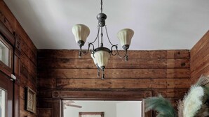 A wooden interior with a chandelier, a rug, a chair, and a dresser.