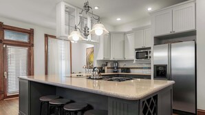 A kitchen with a large island, bar stools, stainless steel appliances, and a window with blinds.