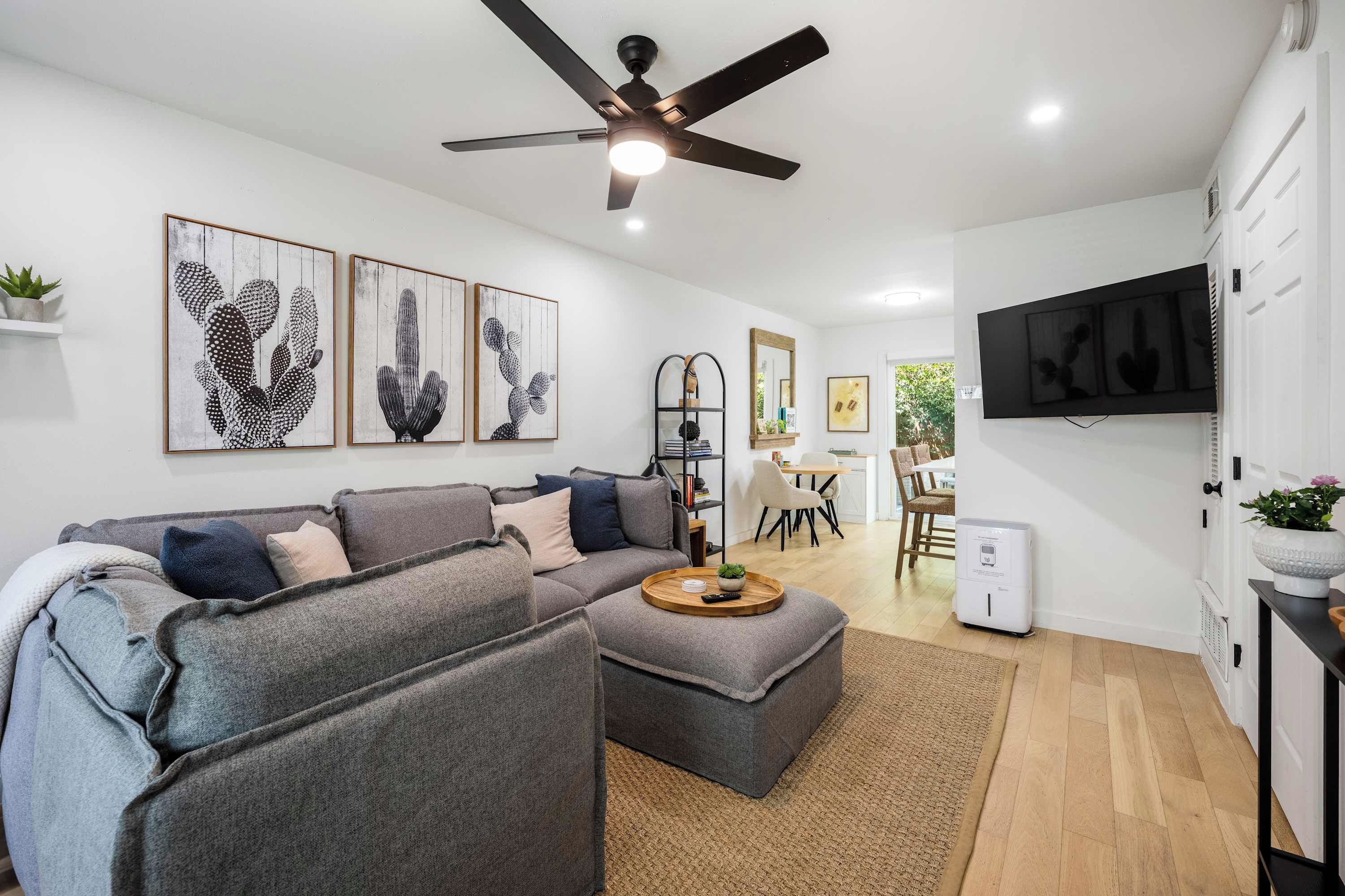 A modern living room with a grey sectional sofa, a ceiling fan, and artwork on the walls.