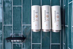 Three bottles of Tarocco body wash on a tiled wall.