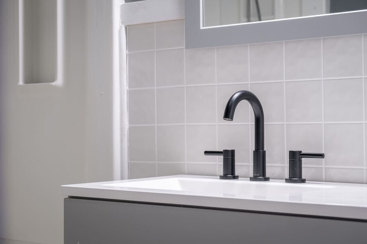A modern bathroom with a white sink, black faucet, and white tiled walls.