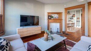 A modern living room with a flat-screen TV, a fireplace, and a dining area visible through an open doorway. - Robin's Egg ~ Private Downtown, Pet-Friendly Gem (Columbus)