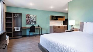 Una camera d'albergo con un letto, una scrivania, una sedia, angolo cottura e un armadio.