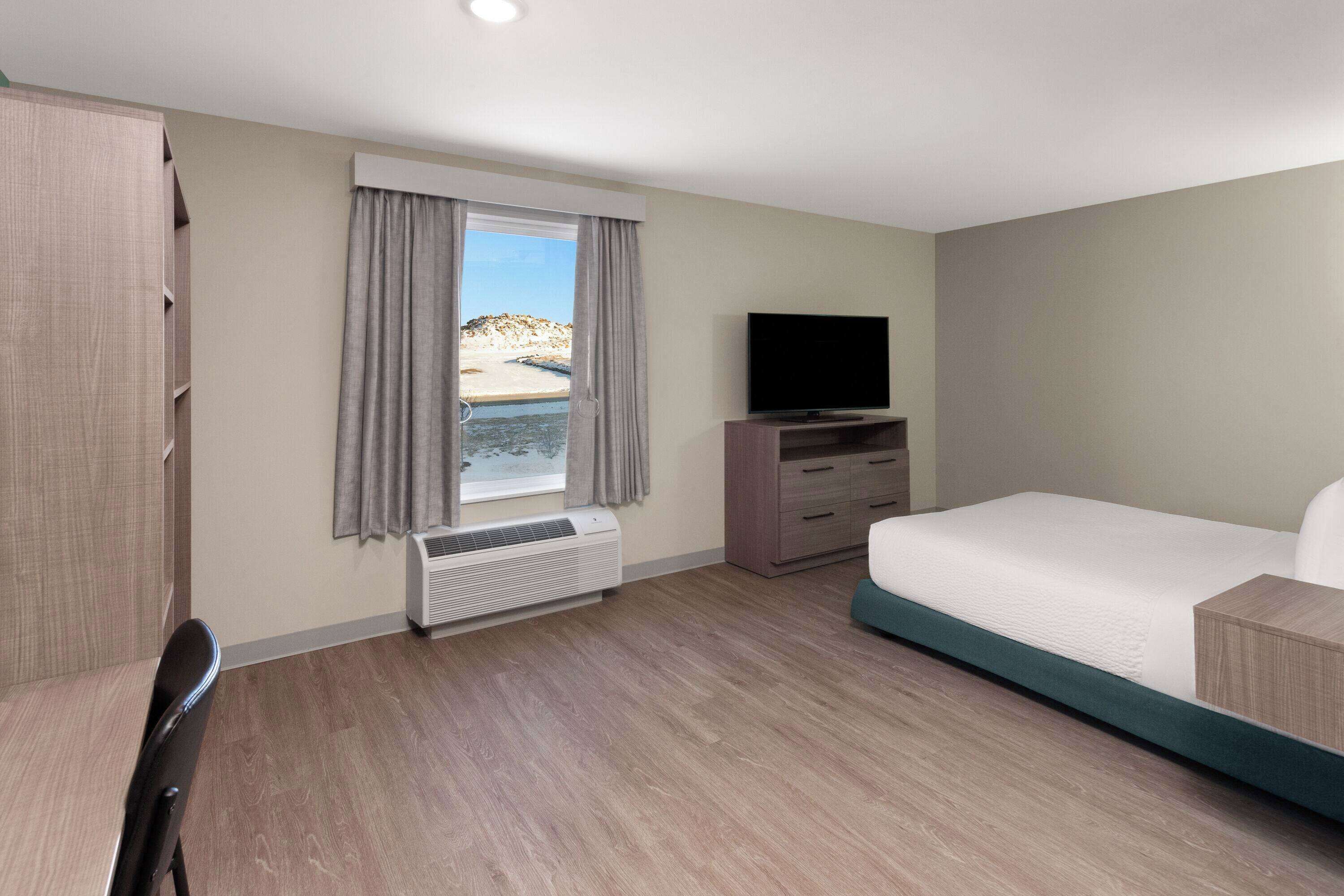 A hotel room with a bed, a TV, a desk, and a window with curtains.
