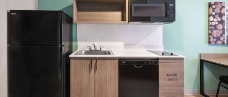 A compact kitchen with a black refrigerator, a microwave, a dishwasher, and wooden cabinets.