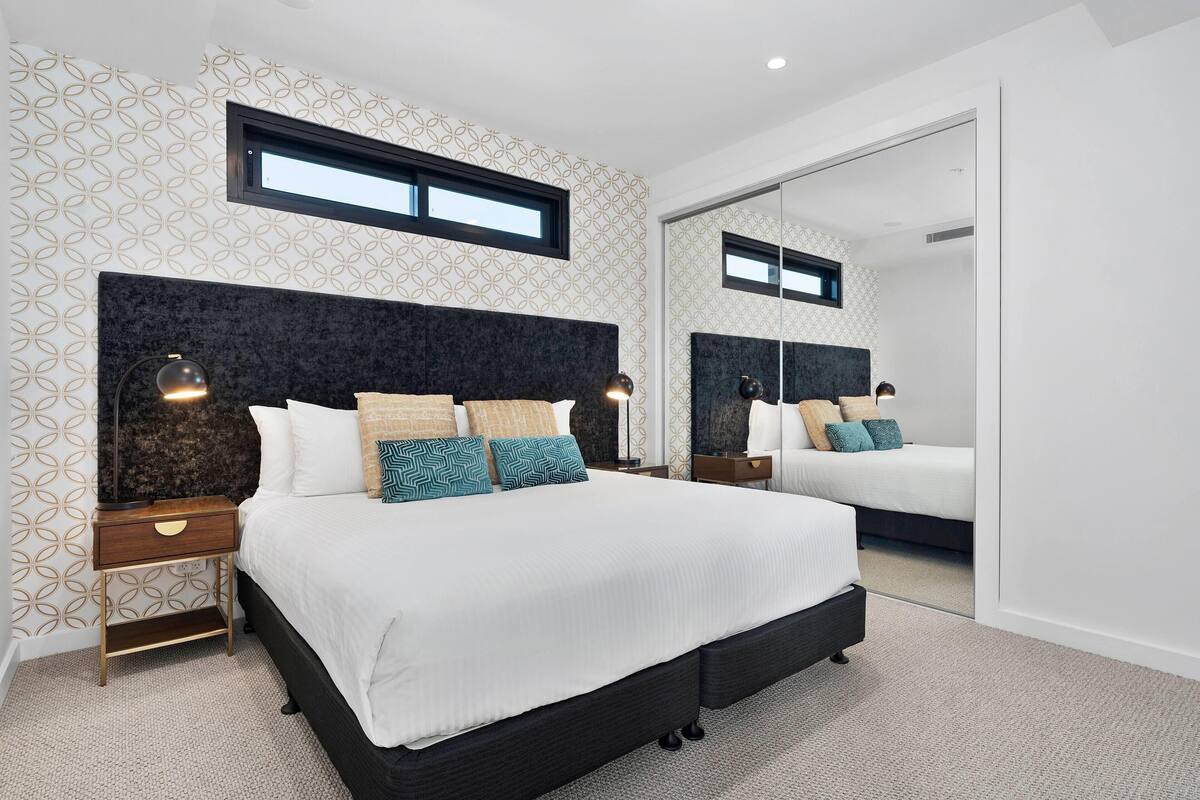 Une chambre moderne avec un grand lit, des tables de chevet, un miroir et un papier peint à motifs.