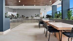 A modern kitchen with stainless steel appliances, a patterned wall, and a dining area with a long table and chairs. - TRYP by Wyndham Southport Gold Coast (Southport)