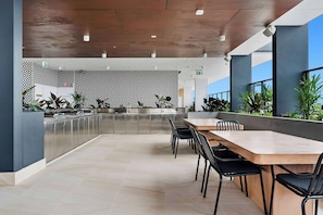 A modern kitchen with stainless steel appliances, a patterned wall, and a dining area with a long table and chairs. - TRYP by Wyndham Southport Gold Coast (Southport)