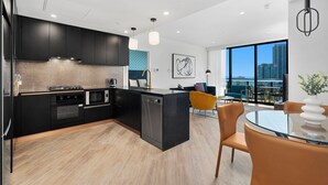 A modern kitchen with black cabinets, a central island, and a dining area with a glass table and yellow chairs.
