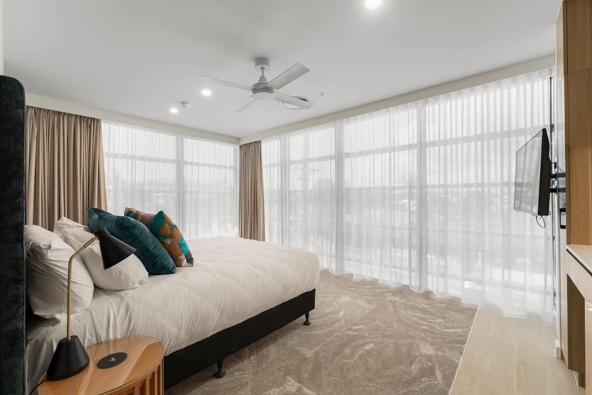Une chambre à coucher moderne avec un grand lit, un ventilateur de plafond et un téléviseur fixé au mur.