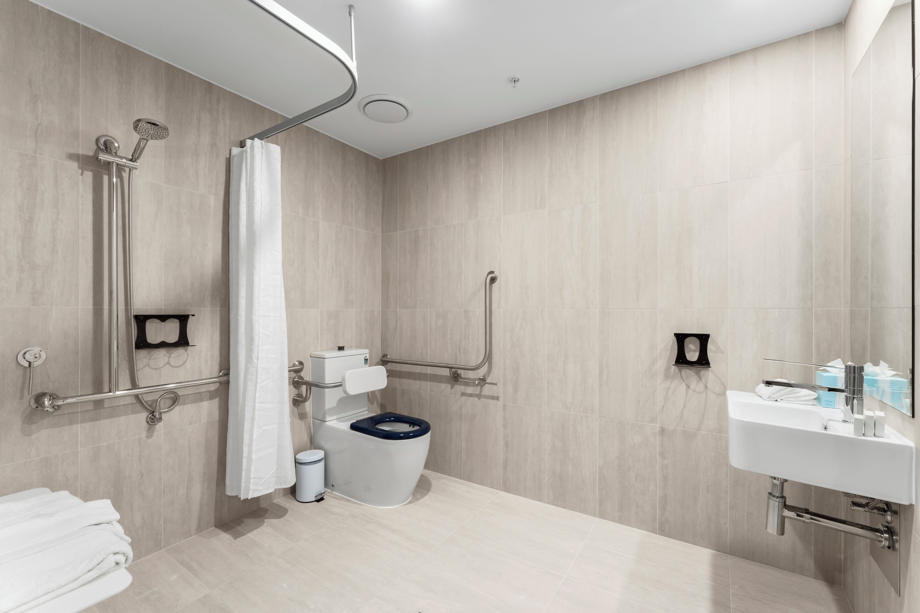Een moderne badkamer met douche, toilet en wastafel, voorzien van handgrepen en een rolstoeltoegankelijke douche.