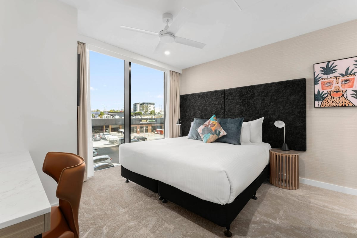 Une chambre d’hôtel moderne dotée d’un grand lit, d’un ventilateur de plafond, d’une vue sur la ville et d’un bureau avec une chaise.