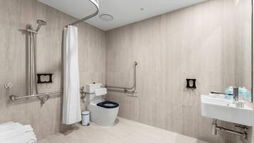 A modern bathroom with a shower, toilet, and sink, equipped with grab bars and a wheelchair-accessible shower.