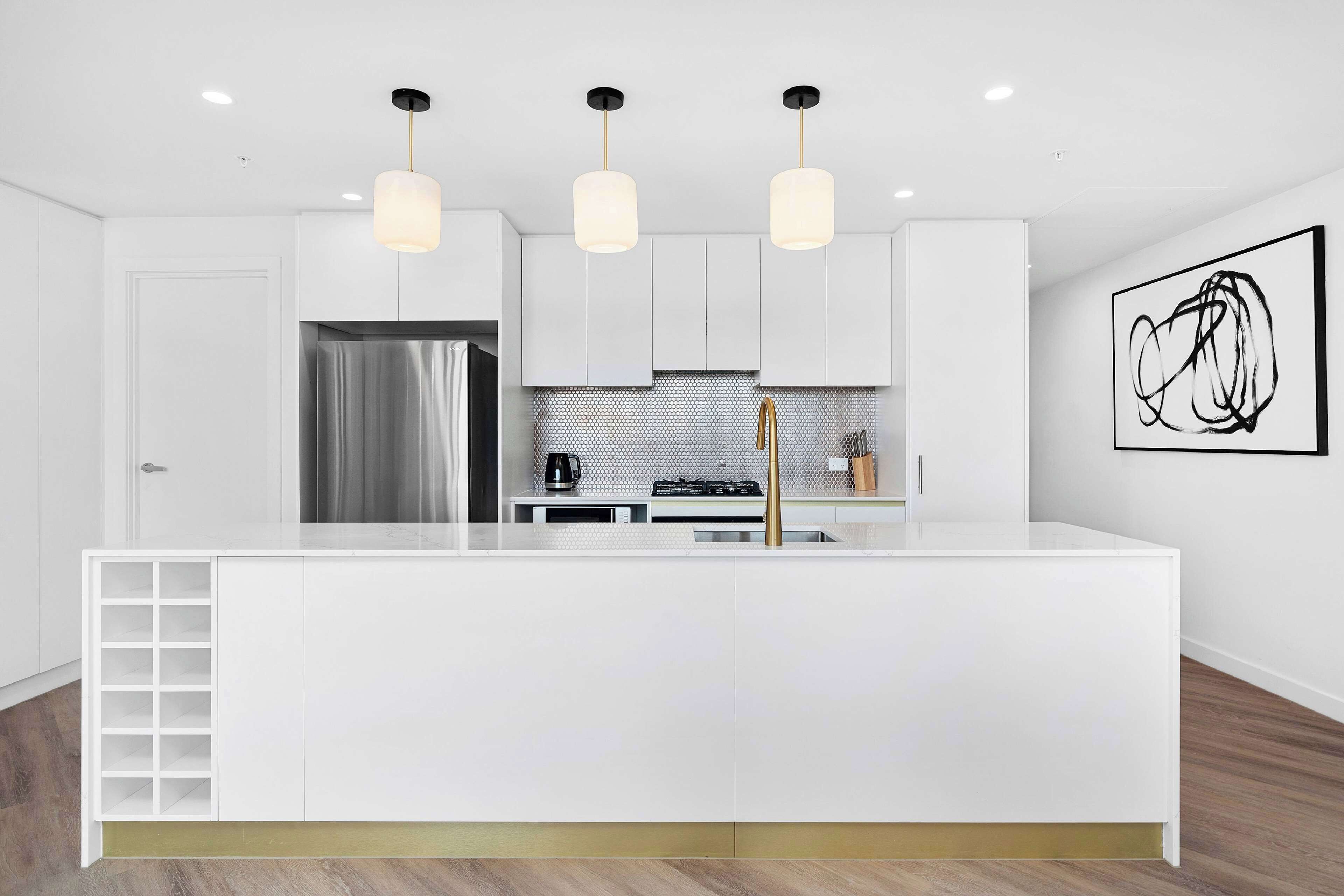 A modern kitchen with white cabinetry, a central island, pendant lighting, and a stainless steel refrigerator.