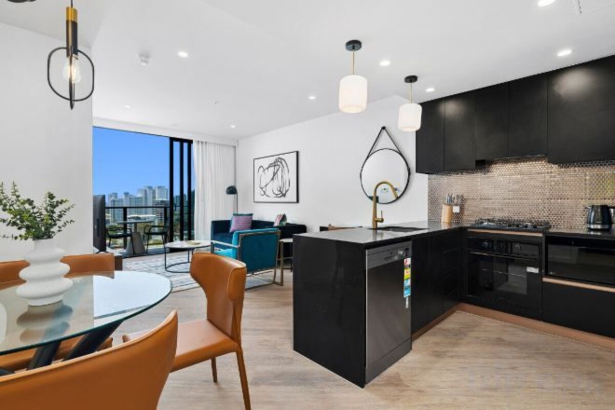 A modern kitchen with a central island, black cabinetry, and a city view through large windows.