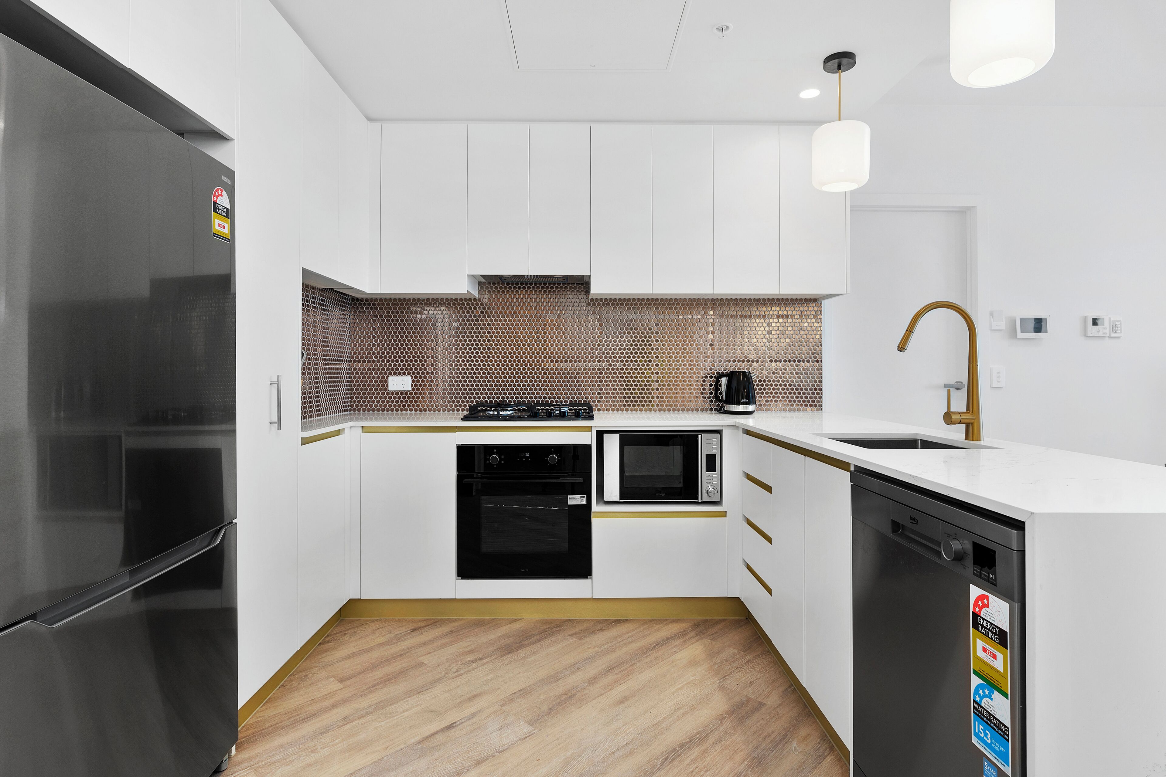 Ett modernt kök med vita skåp, ett kylskåp i rostfritt stål, en mikrovågsugn, en ugn och en diskmaskin.