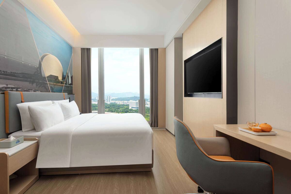 Een hotelkamer met een bed, een bureau, een televisie en uitzicht op een stadsbeeld.