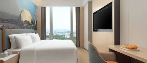 A hotel room with a bed, a desk, a TV, and a view of a cityscape.