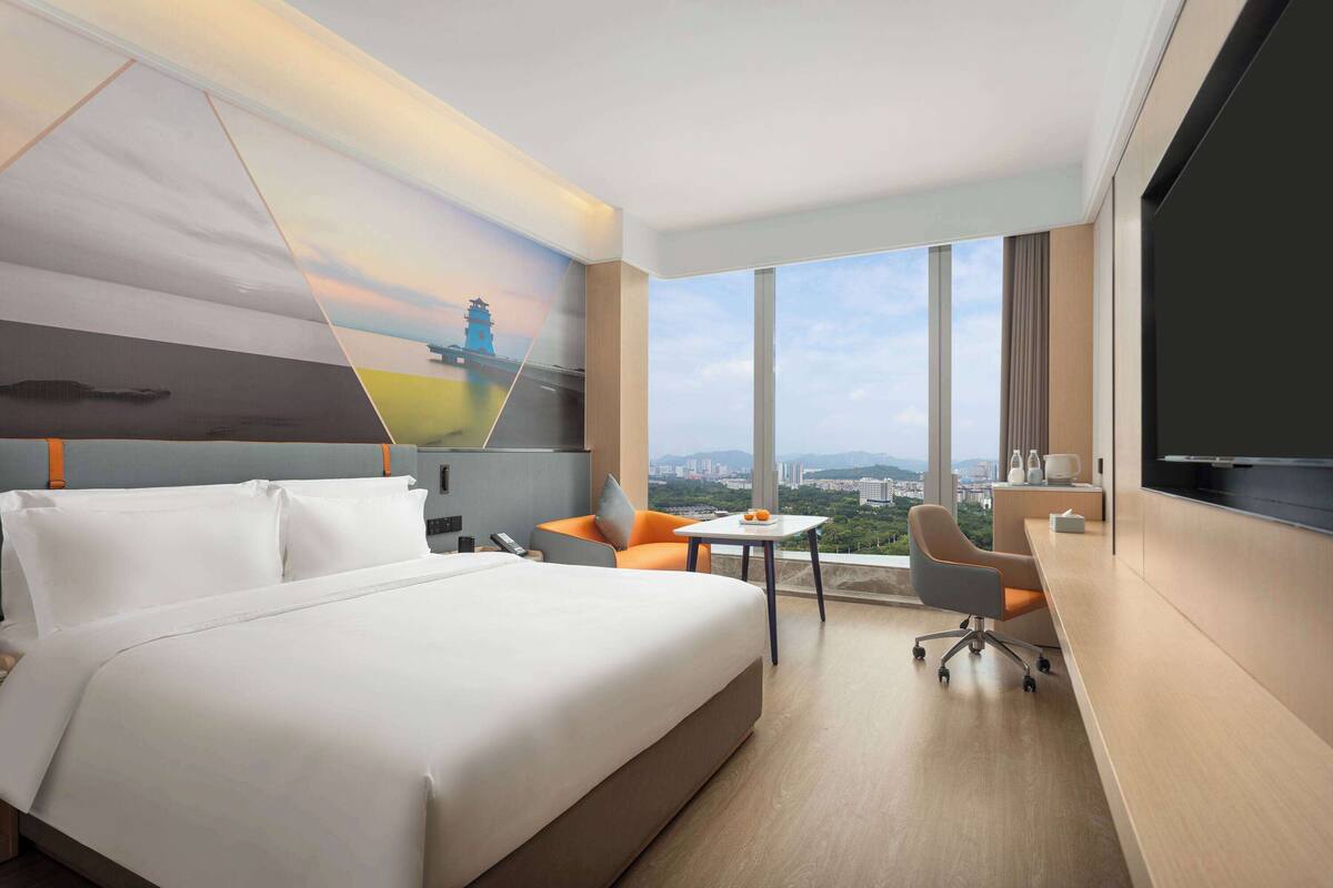 Een hotelkamer met een groot bed, een bureau, een stoel en een televisie. Er is uitzicht op de stad vanuit de ramen.