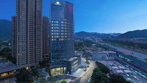 A high-rise hotel with a prominent Days Inn sign, surrounded by urban infrastructure and mountains in the background.