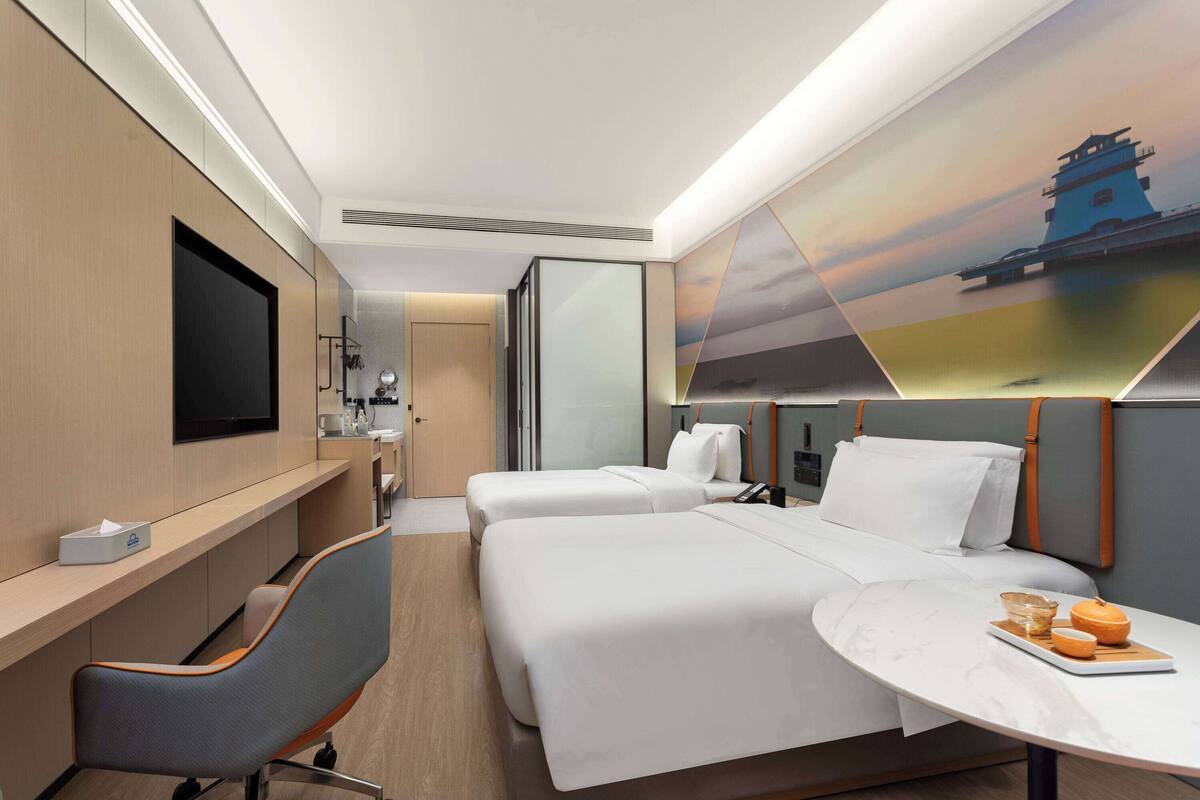Een hotelkamer met twee bedden, een bureau, een stoel, een televisie en een muurschildering.