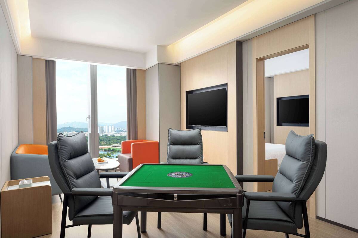 Een moderne kamer met een pooltafel, twee leren fauteuils, een kleine oranje bank en een aan de muur bevestigde televisie.