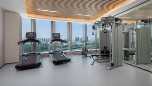A modern gym with treadmills, weight machines, and large windows offering a city view.