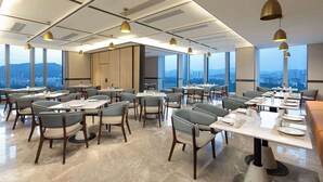 A modern dining area with tables and chairs, large windows, and pendant lighting.
