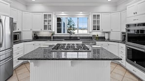 A modern kitchen with white cabinetry, a granite countertop, stainless steel appliances, and a large window with a view of mountains.