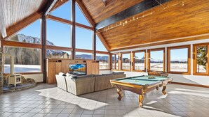 A spacious room with a pool table, a large window offering a mountain view, a fireplace, and a cozy seating area.