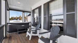 A covered porch with Adirondack chairs and a hot tub.