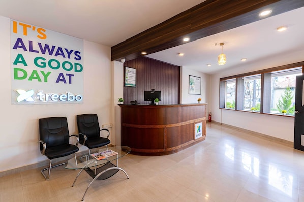 A reception area with a wooden reception desk, two black chairs, a glass table, and a large motivational poster. - Treebo Regalia Comforts, 5 mins to Raja Seat Garden (Madikeri)