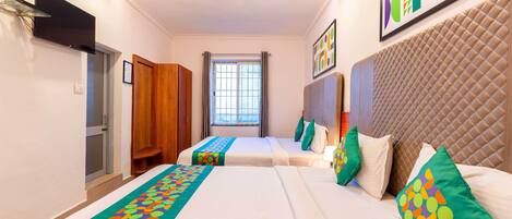 A hotel room with two beds, a ceiling fan, a TV, a window with curtains, and a colorful wall art piece.
