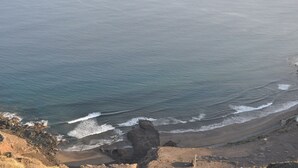 A coastal landscape with a beach, rocky outcrops, and waves approaching the shore.