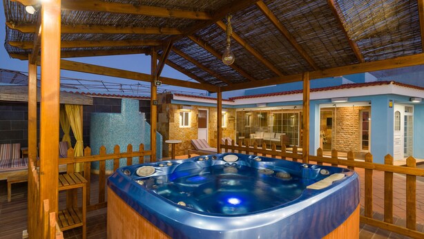 A hot tub in a covered outdoor area with wooden deck and a stone wall.