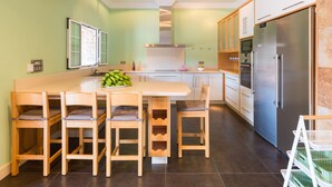 A modern kitchen with a central island, wooden chairs, a stainless steel refrigerator, and light green walls.