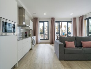 Un apartamento moderno con cocina, un sofá gris y ventanas grandes.