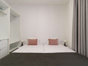 Habitación de hotel con cama, dos mesitas de noche, un armario y una cortina.